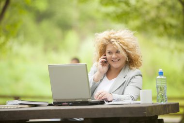 Woman using mobile phone and laptop in open office clipart