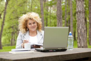 Woman using laptop in park on wooden table clipart