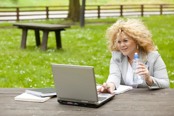 使用便携式计算机在公园和喝水的女人 — 图库照片