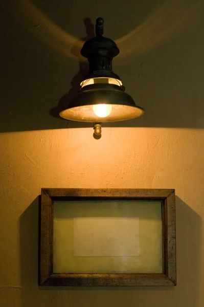 Old lamp is hanging over empty picture frame — Stock Photo, Image