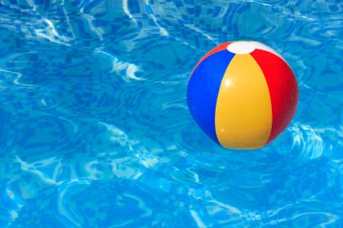 A colorful beach ball floating in a swimming pool clipart