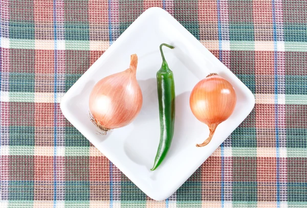 Pimenta de pimentão verde e duas cebolas em um prato branco Fotos De Bancos De Imagens