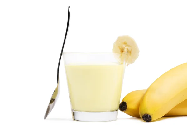 Bananen-Milchshake mit einem Stück Banane, einem Löffel und Bananen zur Seite — Stockfoto