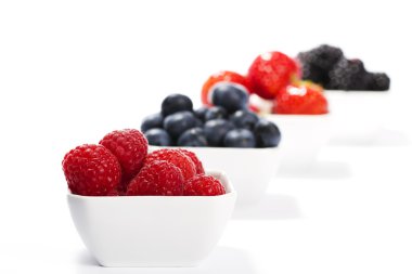 Raspberries in front of wild berries in bowls clipart