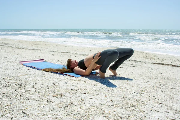 Žena, která dělá jóga cvičení na pláži v póza most — Stock fotografie