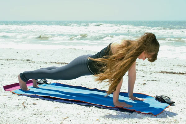 Vrouw doen yoga oefening op strand in hoge plank pose — Stockfoto