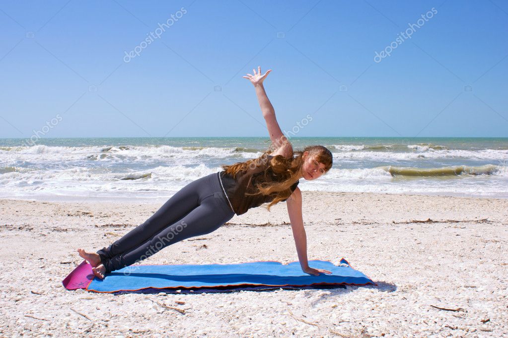 Young woman doing yoga exercise on beach in Vasisthasana or side