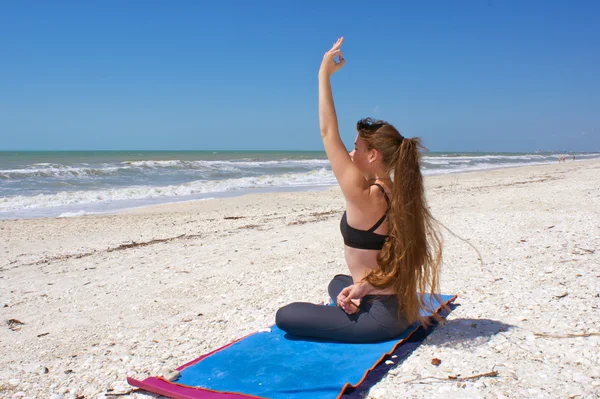 Mulher fazendo exercício de ioga na praia em meia pose de lótus encadernada ou A — Fotografia de Stock