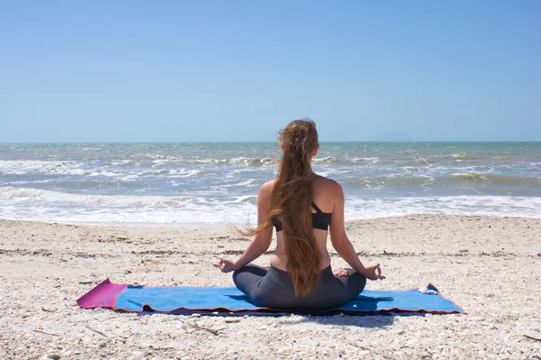 Žena, která dělá jóga cvičení na pláži v polovičním lotosu pozice nebo ardha p — Stock fotografie