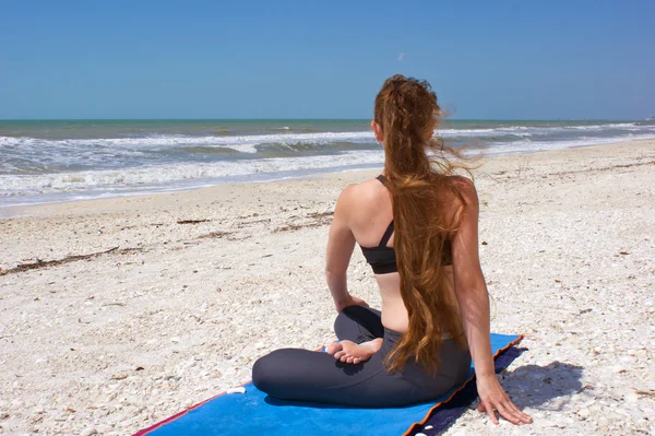 Vrouw doen yoga oefening op strand in gedraaid helft lotus pose of — Stockfoto
