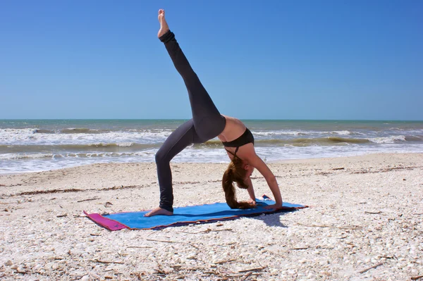 Kobieta robi joga ćwiczenia jednej nodze pełne koła poza na plaży — Zdjęcie stockowe