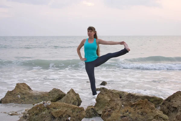 Kvinnan gör yoga övning stående hand till tå posera i vatten vid — Stockfoto