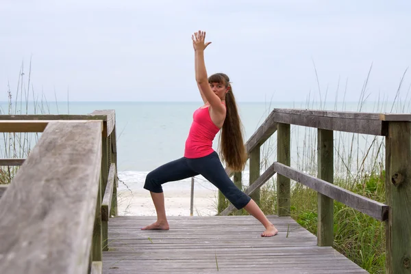 Vrouw doen yoga oefening warrior 1 pose op de promenade bij strand d — Stockfoto