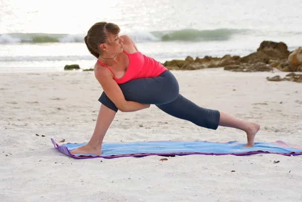 Женщина на пляже на закате делает упражнения йоги связаны расширенный угол позы — стоковое фото