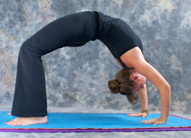 Woman doing yoga exercise full wheel pose on on mat in studio clipart