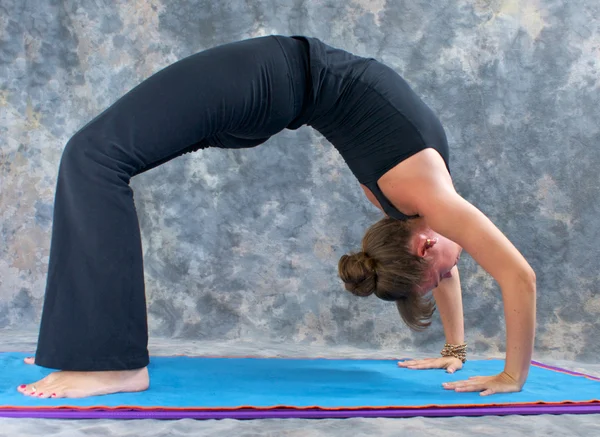 Vrouw doen yoga oefening volledige wiel pose op op mat in studio — Stockfoto