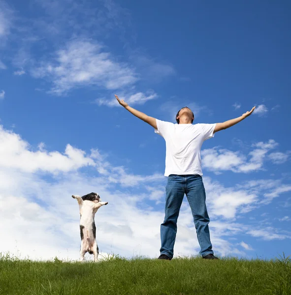 Молодой человек отдыхает на зеленом поле со своей собакой — стоковое фото