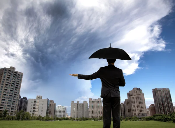 Бизнесмен в темных апартаментах с зонтиком и наблюдает за штормом — стоковое фото