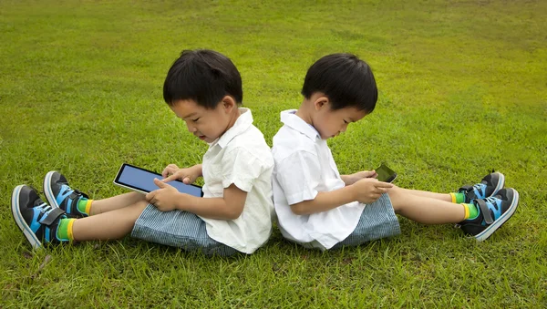Dwoje dzieci za pomocą ekranu dotykowego komputera typu tablet pc na trawie — Zdjęcie stockowe