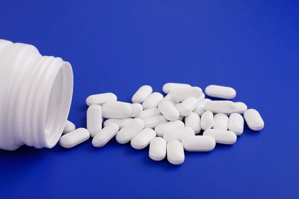 Comprimidos derramados e frasco de medicamento.Comprimidos sobre fundo azul — Fotografia de Stock
