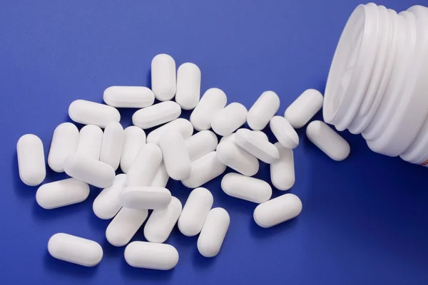 Comprimidos derramados e frasco de medicamento. Comprimidos em um fundo azul — Fotografia de Stock