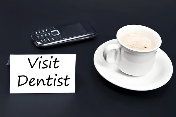 Besöka tandläkare meddelande på skrivbord med kaffe — Stockfoto
