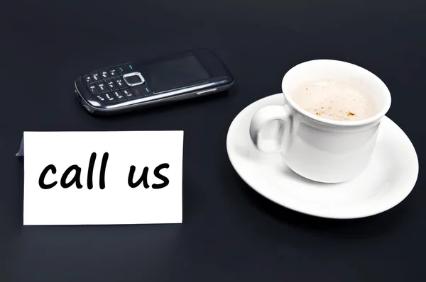 Зателефонуйте нам, помічені на столі з кавою — стокове фото