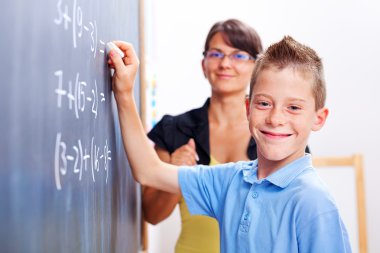 Boy standing on chalkboard in front of teacher clipart