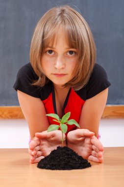 Serious elementary schoolgirl protecting plant clipart