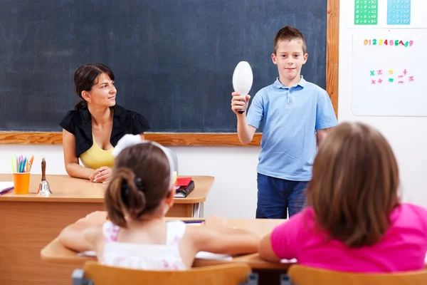 Школьник держит лампочку перед классом — стоковое фото