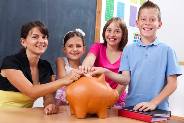 Schüler und Lehrer stecken Münze in Sparschwein — Stockfoto