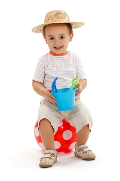 Liten pojke sitter på prickade boll, hålla sandlåda leksaker — Stockfoto