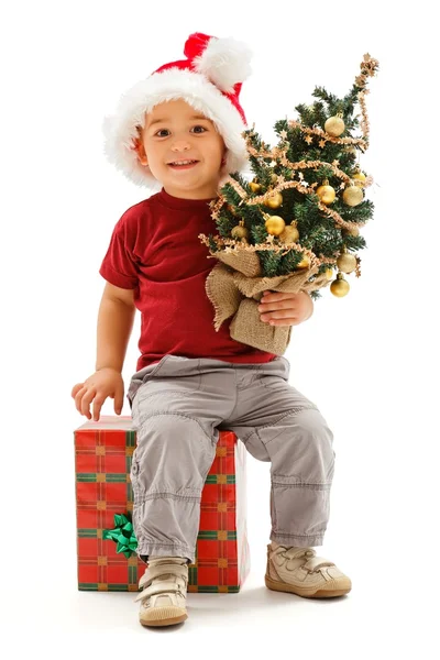 Lilla jul pojke sitter på närvarande, håller granen — Stockfoto