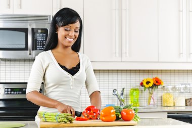 Young woman cutting vegetables in kitchen clipart