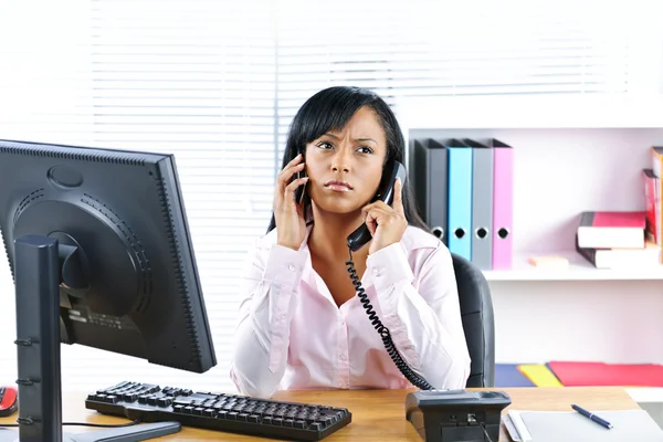 Czarna kobieta za pomocą dwóch telefonów na biurko — Zdjęcie stockowe