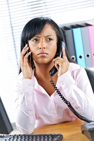 Empresaria negra usando dos teléfonos en el escritorio —  Fotos de Stock