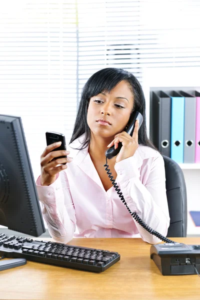 黑色女商人在办公桌上使用两个手机 — 图库照片