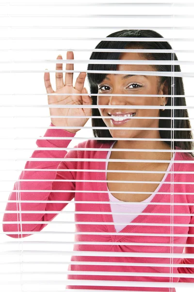 Mulher sorridente olhando através de persianas — Fotografia de Stock