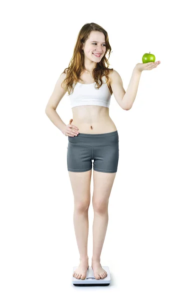 Молодая улыбающаяся девушка на весах в ванной держит яблоко — стоковое фото