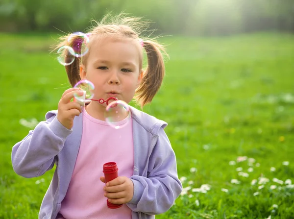 Kleines Mädchen pustet Seifenblasen auf Wiese — Stockfoto