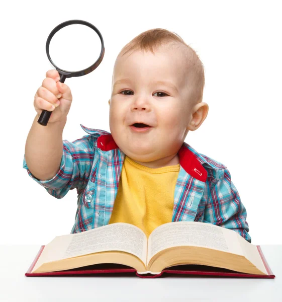 Маленький ребенок играет с книгой и лупой — стоковое фото