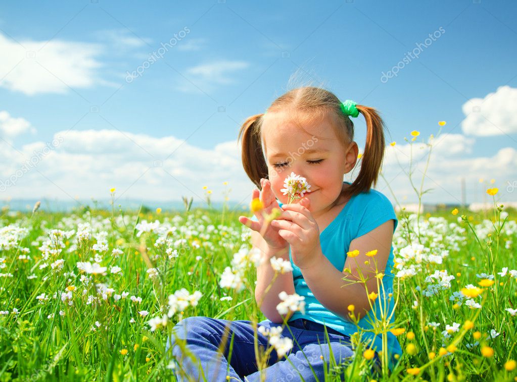 Little girl is smelling flowers on green meadow