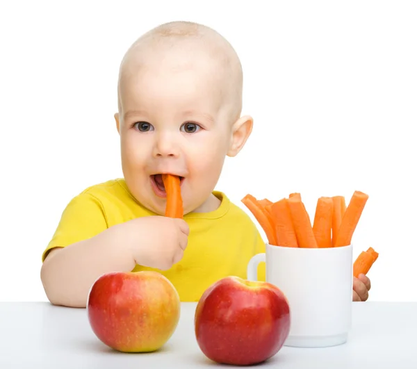 Милий маленький хлопчик їсть моркву та яблука — стокове фото