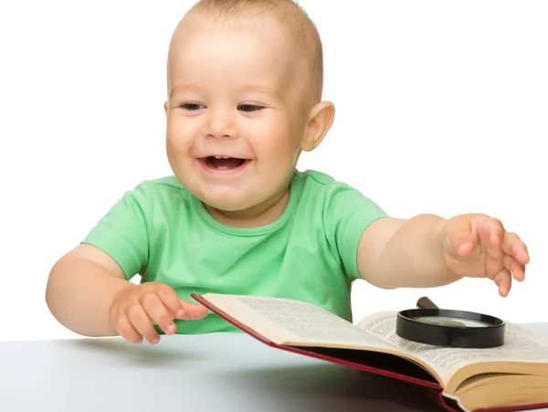 Niño pequeño juega con el libro y la lupa —  Fotos de Stock