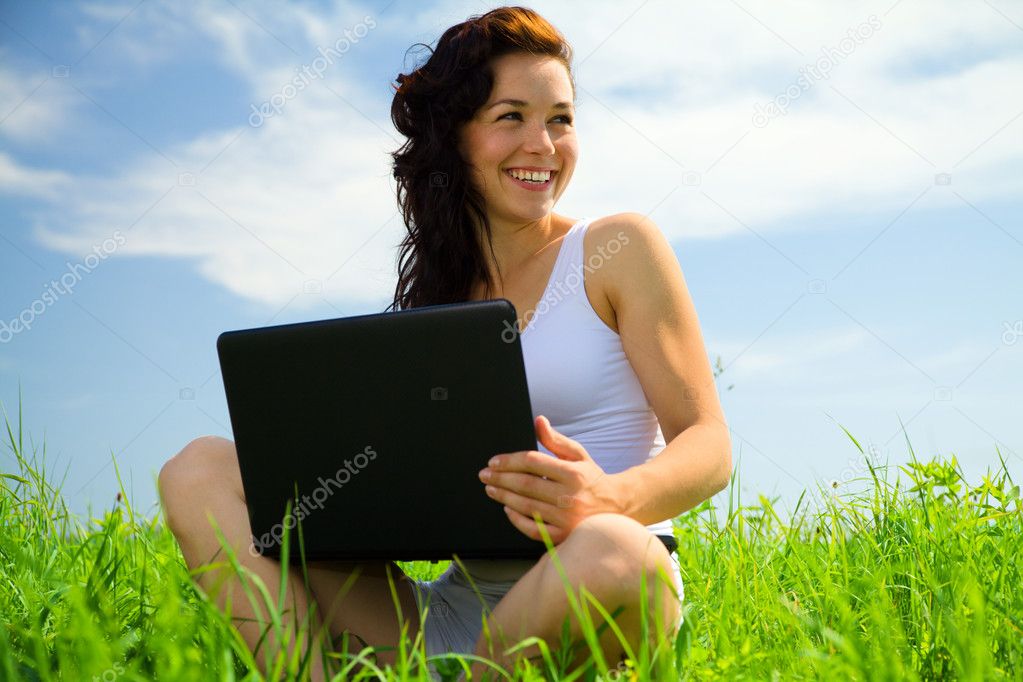Cute girl is sitting on green grass with laptop