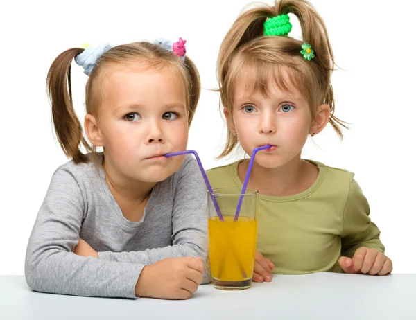 Две маленькие девочки пьют апельсиновый сок — стоковое фото