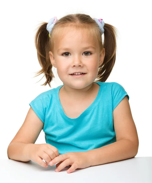 A menina feliz está sentada à mesa — Fotografia de Stock