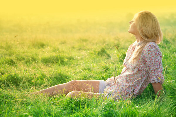 Beautiful girl is relaxing while sitting on green field