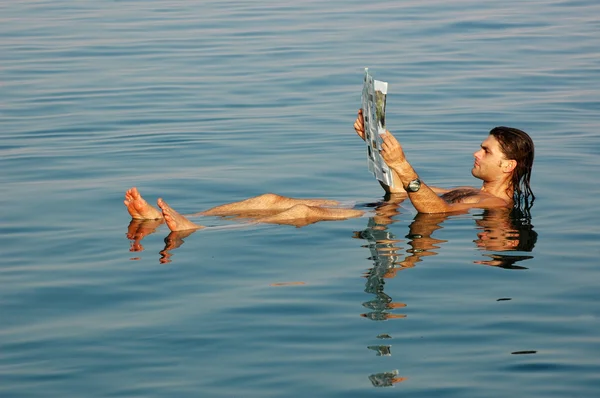 Homem flutuando em um mar morto com jornal — Fotografia de Stock