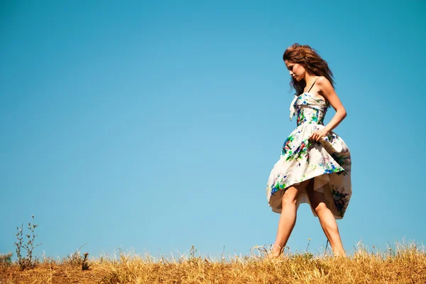 Kvinnan promenader genom gräs, blå himmel i bakgrunden — Stockfoto